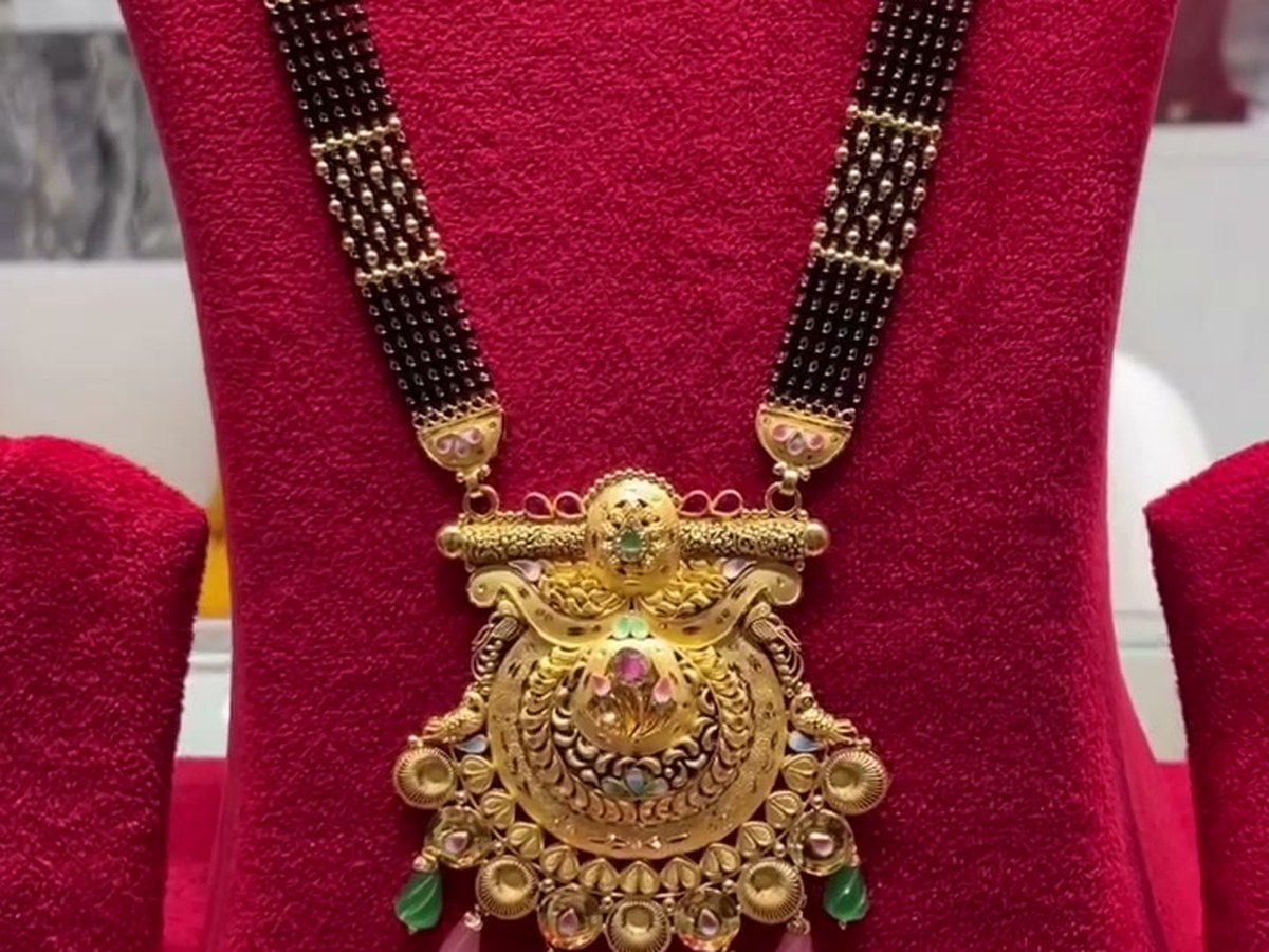 A 22K gold mangalsutra with black beads and a detailed pendant on red cloth